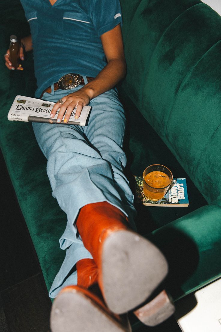 a man sitting on a green couch with his feet up and holding a book in front of him