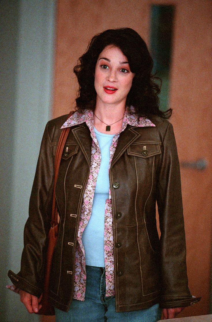 a woman wearing a brown leather jacket and blue shirt is standing in front of a door