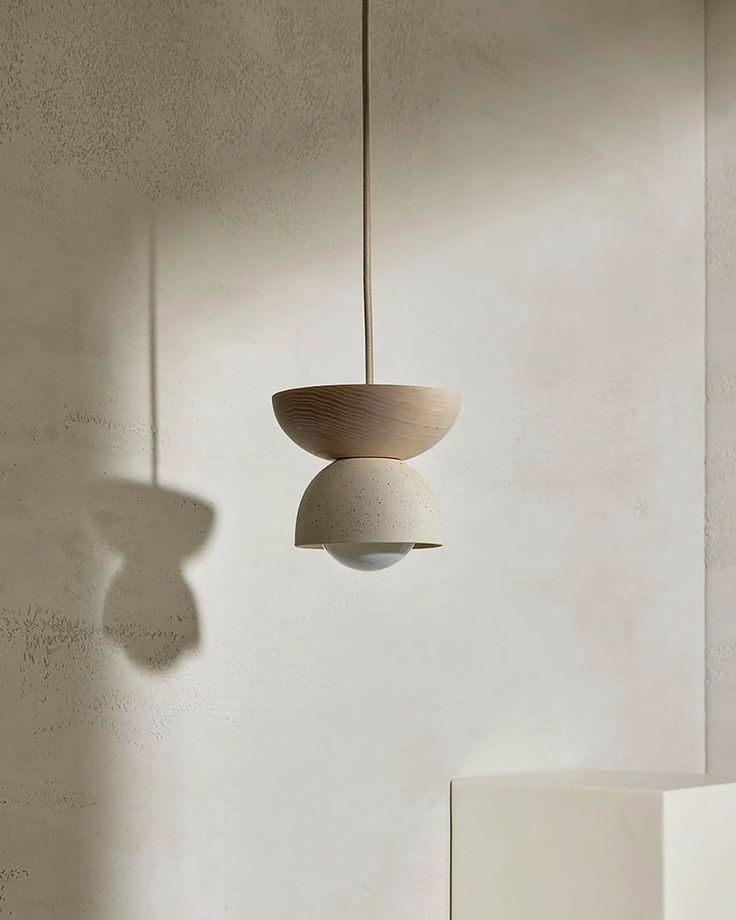 a light fixture hanging from the side of a wall next to a white vase on a table