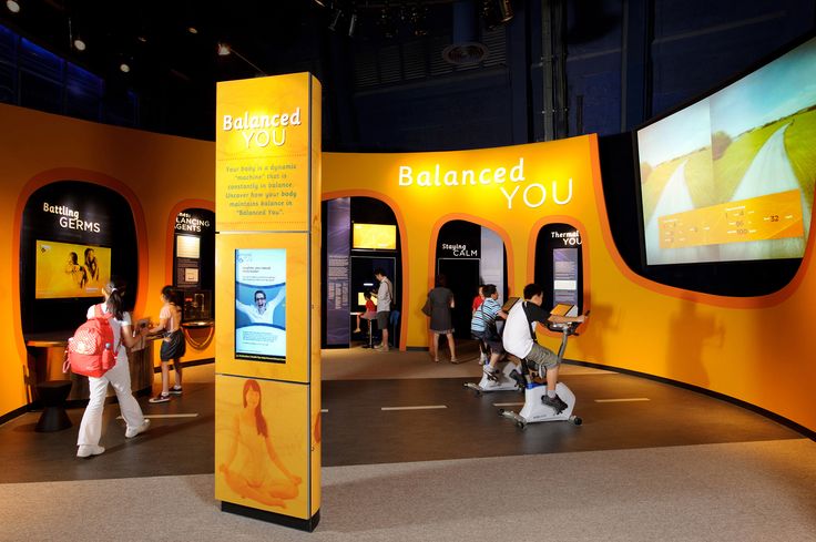 people are walking around in an exhibit with orange walls and large screens on the wall