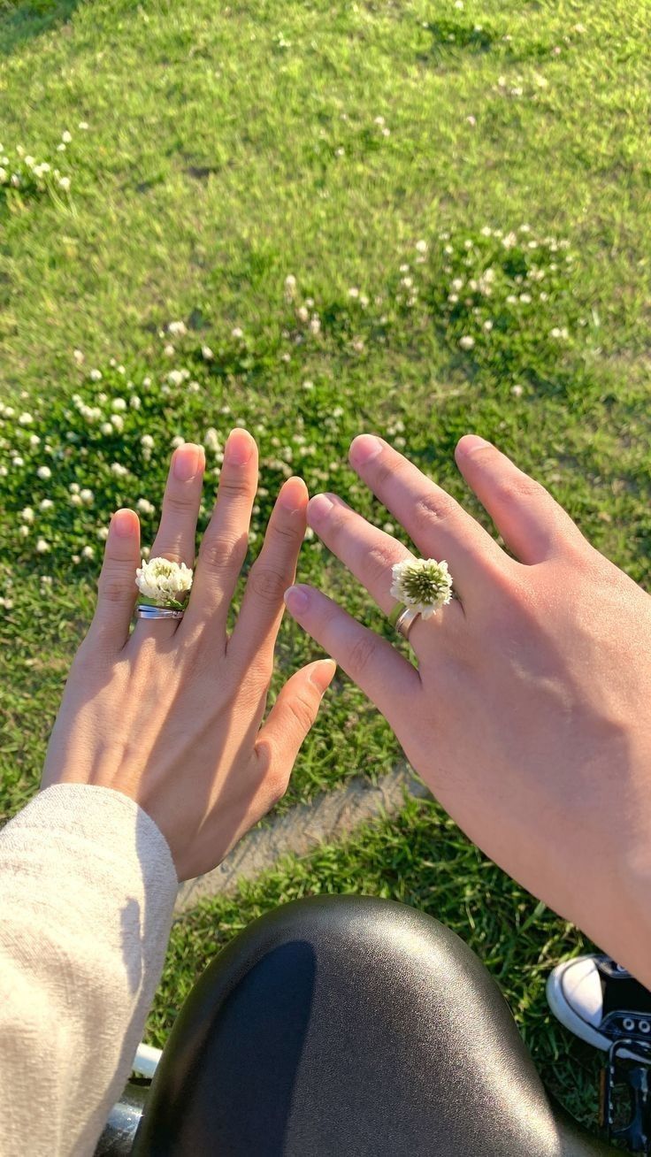 two people with their hands on each other's fingers, sitting in the grass