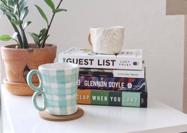 a stack of books sitting on top of a table next to a coffee cup and plant