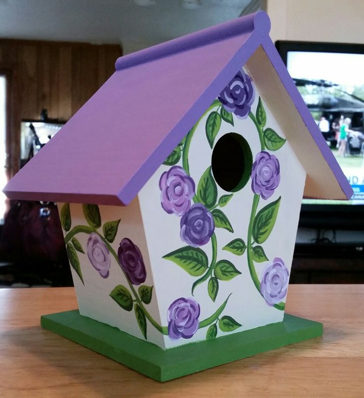 a birdhouse painted with purple flowers and green leaves on the outside, sitting on a table in front of a television