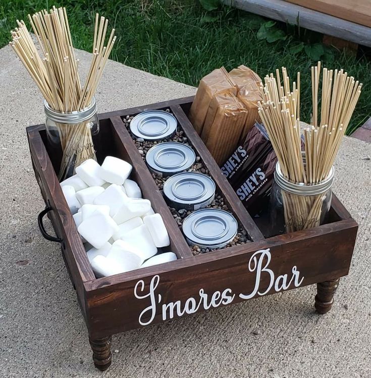 a wooden tray filled with marshmallows, candles and other items on concrete