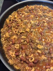 a large skillet filled with chili and macaroni noodles on top of a stove