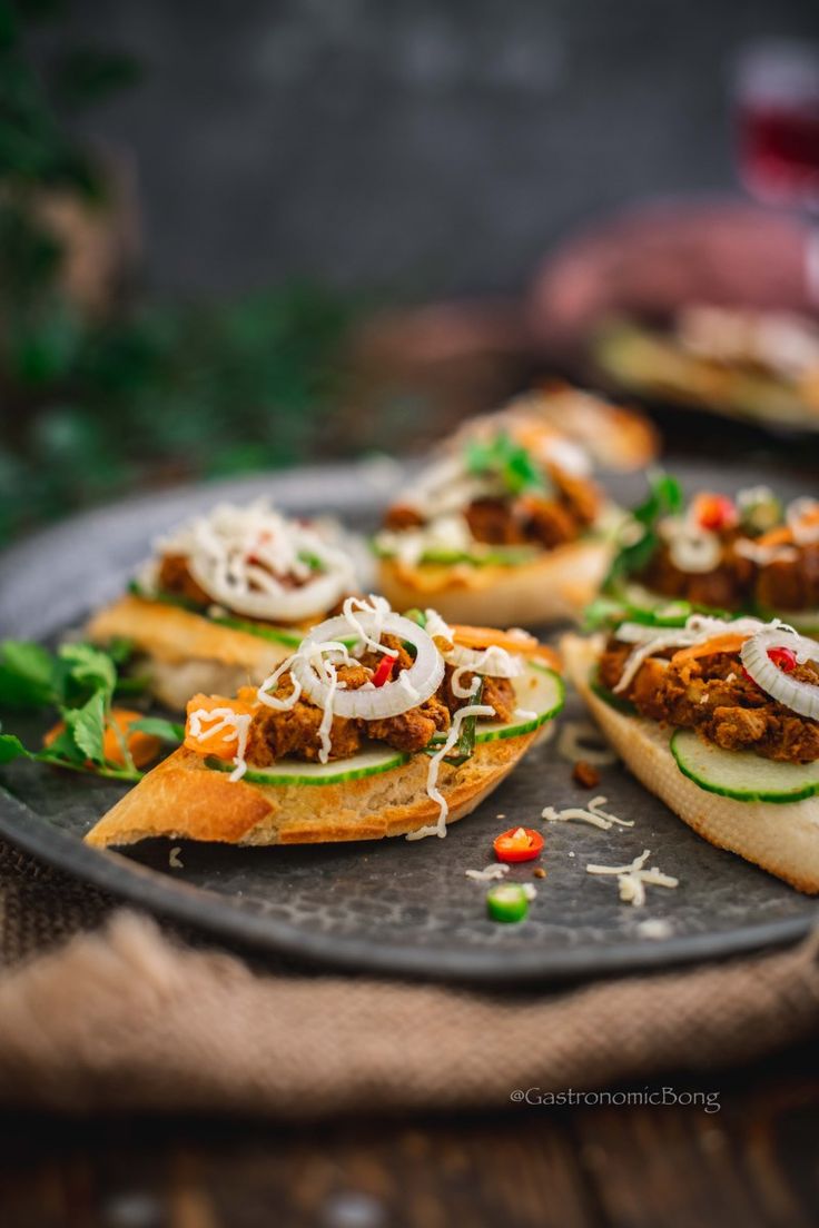 small sandwiches with meat, cheese and veggies are on a black platter