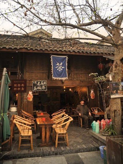 an outdoor restaurant with wooden chairs and tables in front of the building that has chinese writing on it