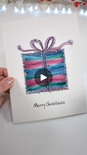 someone holding up a christmas card with a gift on it