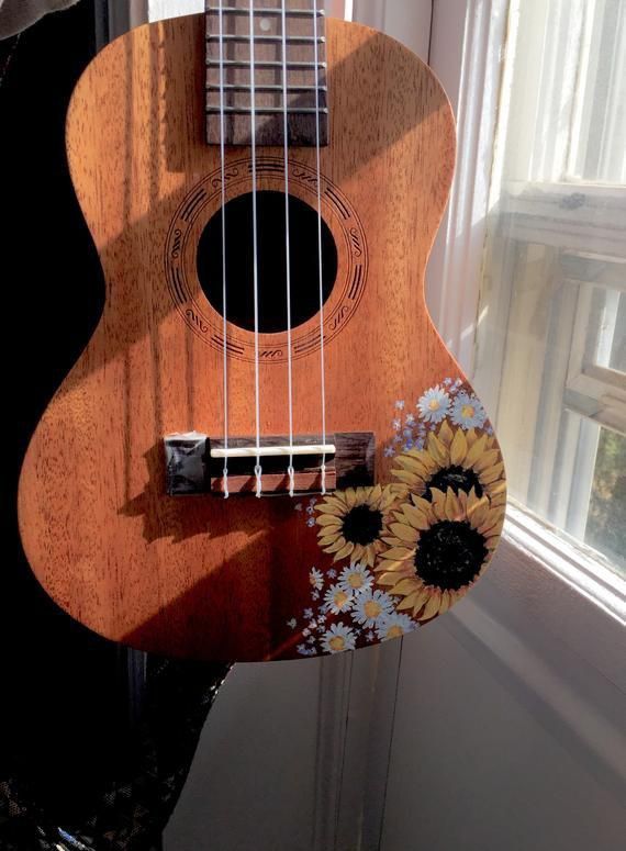 a ukulele with sunflowers painted on it sitting in front of a window