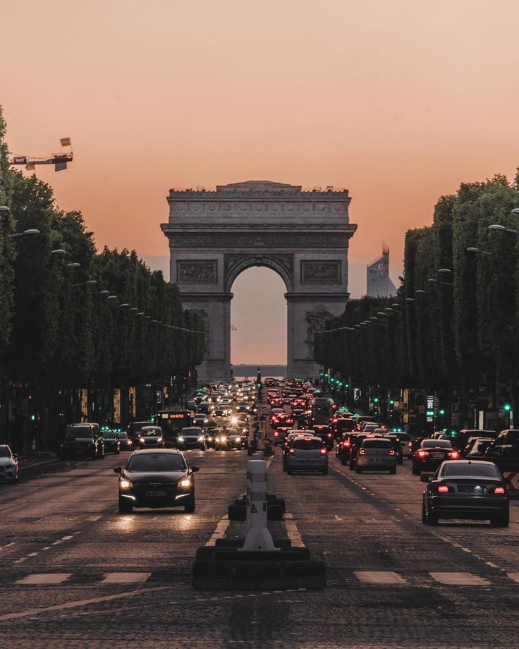 cars are driving down the street in front of an arc de trioe at dusk