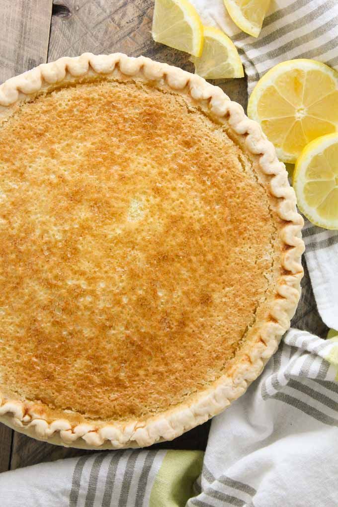 a pie with lemons around it on top of a wooden table next to napkins