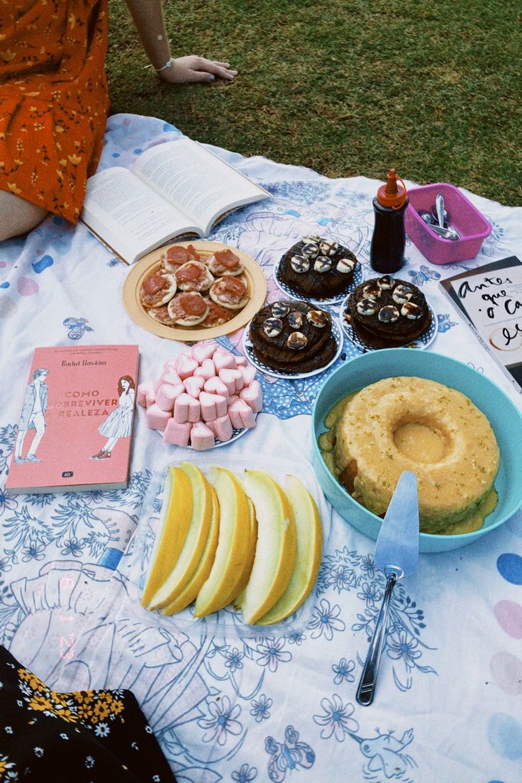 a table topped with cakes and desserts on top of a grass covered field next to a book