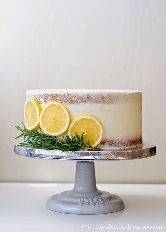 a white cake with lemons and rosemary on top, sitting on a silver pedestal