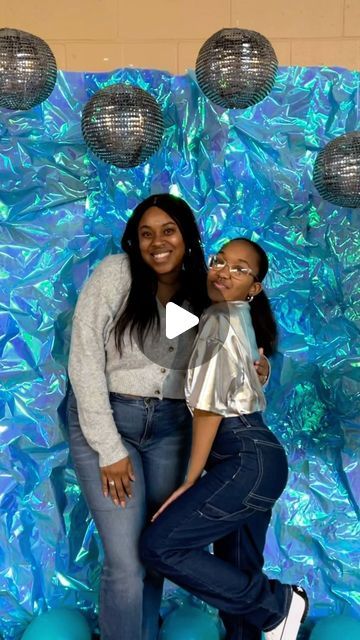 two women pose for a photo in front of a backdrop with disco balls and lights