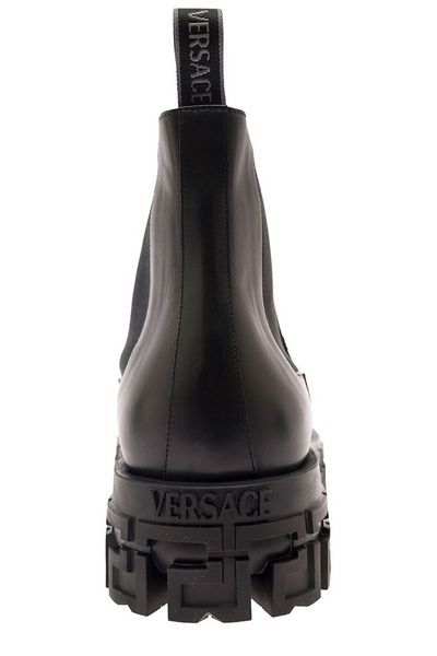 Elevate your style with the GRECA PORTICO Chelsea Boots by Versace. Crafted in smooth leather, these ankle boots are a luxurious addition to any wardrobe. The thick rubber lug sole featuring the iconic Greca pattern adds a touch of elegance to the edgy design. With side elastic inserts, logoed back pull, and a leather interior, these boots offer both comfort and style, making them the perfect choice for fashion-forward individuals. Smooth leather construction Thick rubber lug sole with Greca pat Luxury Ankle Combat Boots With Lug Sole, Luxury Platform Boots With Lug Sole, Streetwear Ankle Heeled Boots With Lug Sole, Calf Leather Chelsea Boots With Vibram Sole, Black Chelsea Boots With Lug Sole In Calf Leather, Luxury Ankle Moto Boots With Lug Sole, Black Calf Leather Chelsea Boots With Lug Sole, Black High-top Chelsea Boots In Calf Leather, High-top Calf Leather Boots For Streetwear