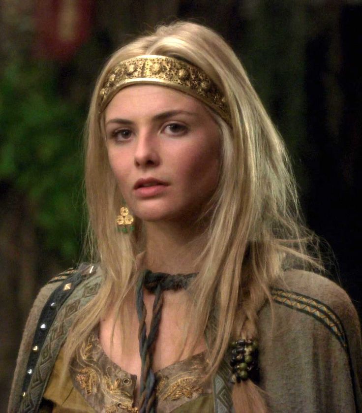 a woman with long blonde hair wearing a gold headband and a brown dress is looking at the camera