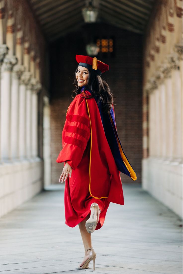 a woman in a red graduation gown and cap is walking down the street with her hand on her hip