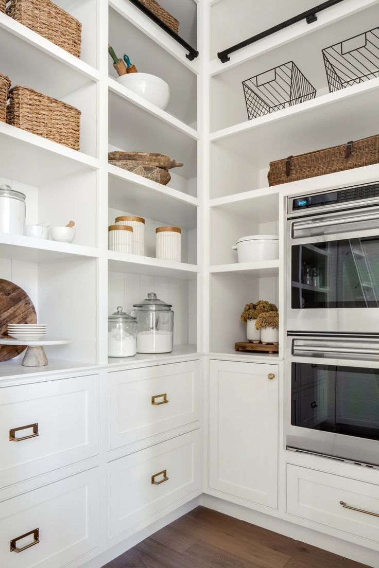 a white kitchen with open shelving and an oven in the center, along with baskets on the shelves