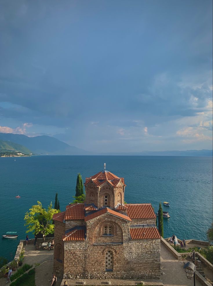 an old church sits on the edge of a cliff by the ocean with people walking around it