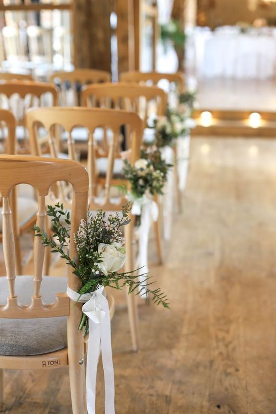 rows of wooden chairs with white flowers and greenery tied to them