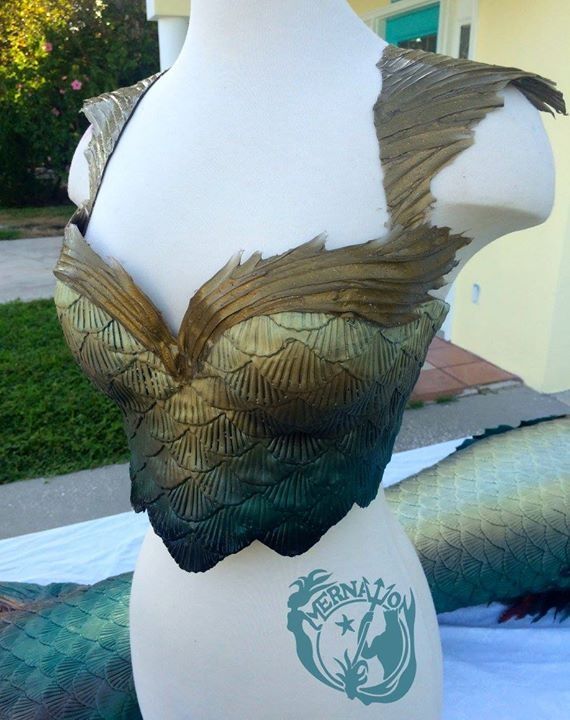 a white mannequin with green and gold leaves on it's bust, in front of a house