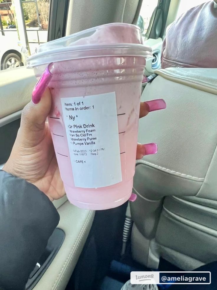 a person holding up a pink drink in the back seat of a car with a sticker on it