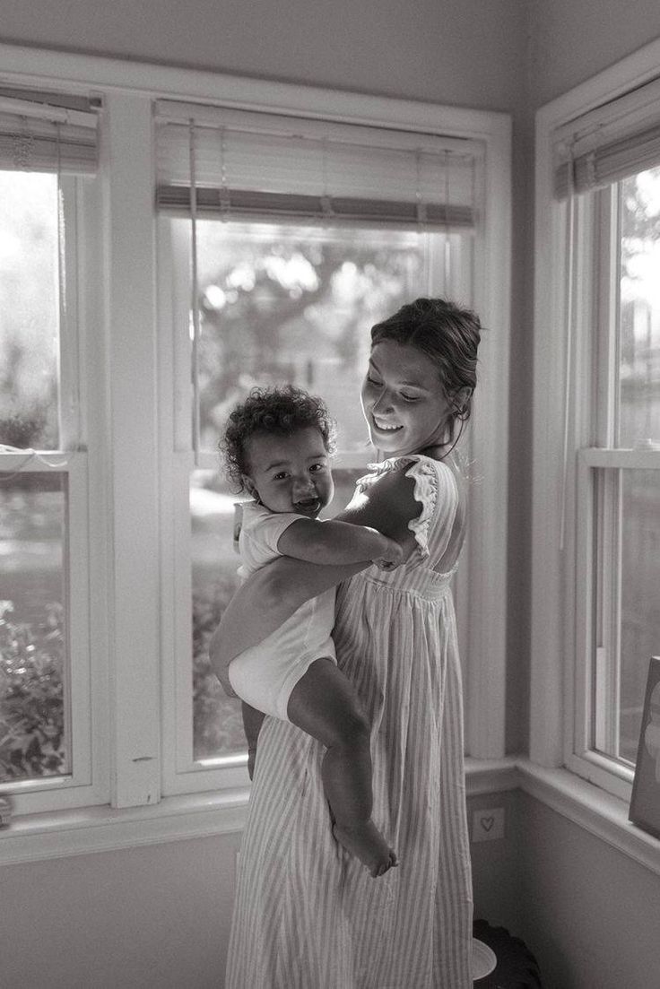 a woman holding a baby in front of a window