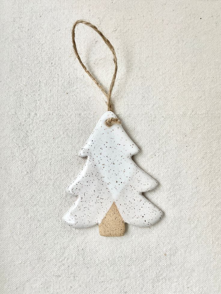 a white ceramic ornament hanging from a string on a white background with a tree decoration