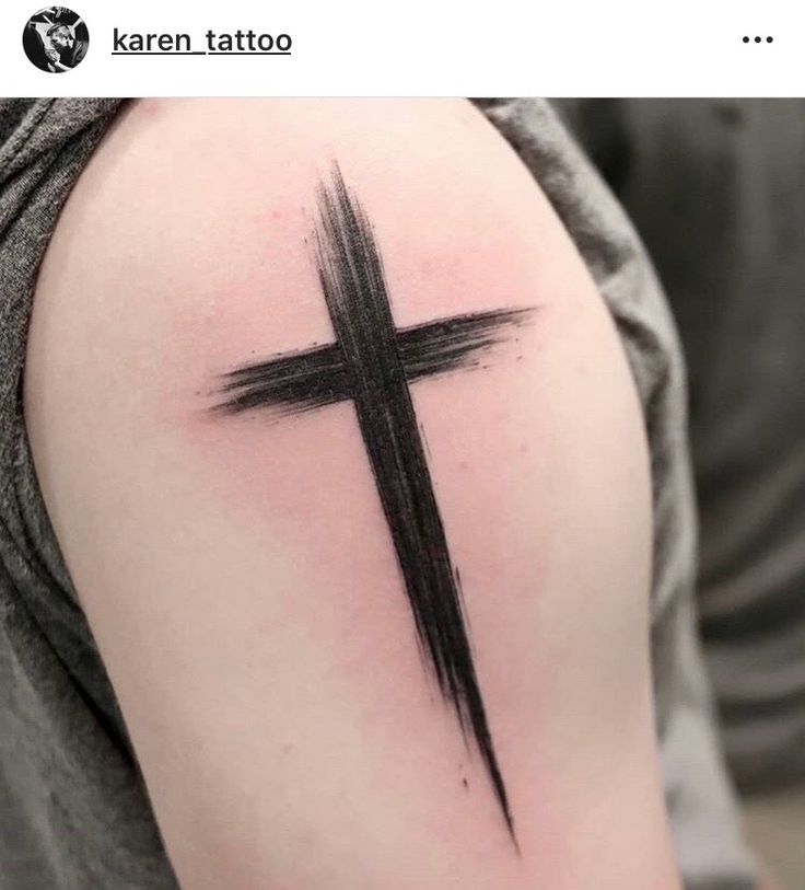 a cross tattoo on the upper arm and shoulder is shown with black ink in it