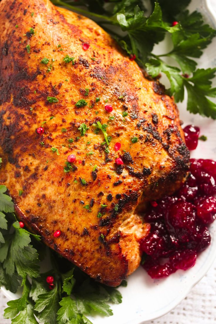 a white plate topped with meat covered in cranberry sauce and garnished with parsley