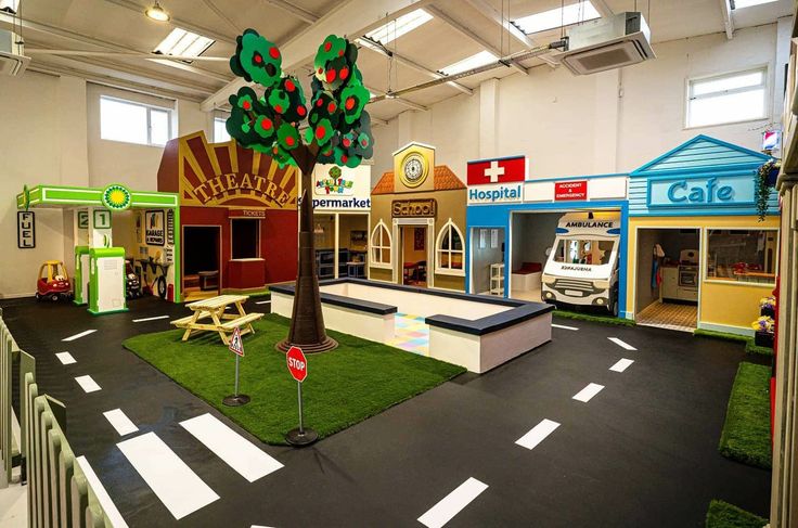 an indoor play area for children with toys on the ground and trees in the center