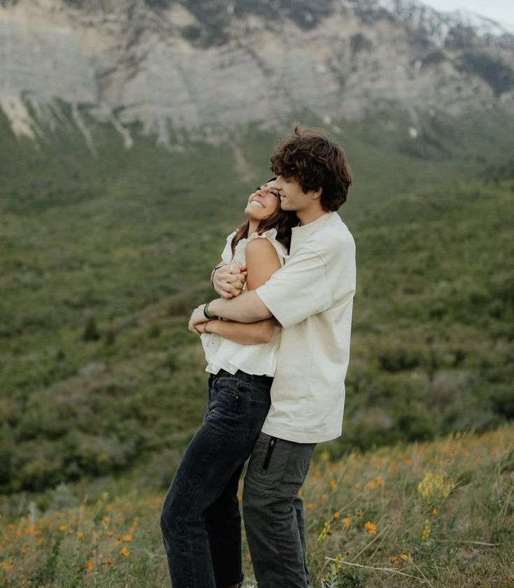 a man and woman embracing each other in front of a mountain with wildflowers