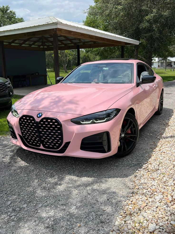 a pink sports car parked in front of a carport with two cars behind it