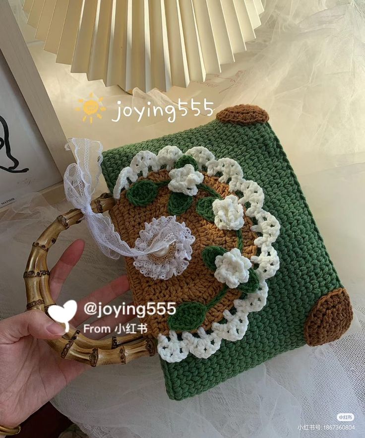 a hand holding a crocheted purse with flowers on the front and side,