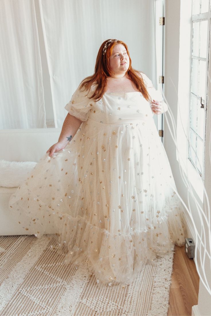 a woman in a white dress is standing near a window with her hands on her hips