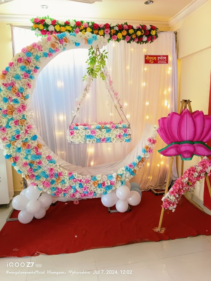 an arch decorated with flowers and balloons in the shape of a flower swing for a baby's first birthday party