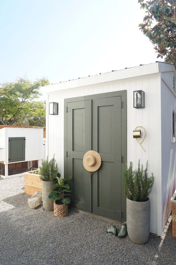 a garden shed with two plants and a hat on the door