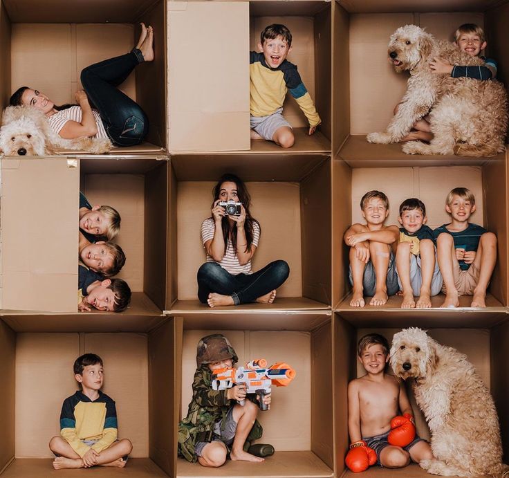 a group of children and their dog sitting in cardboard boxes with one boy holding a camera