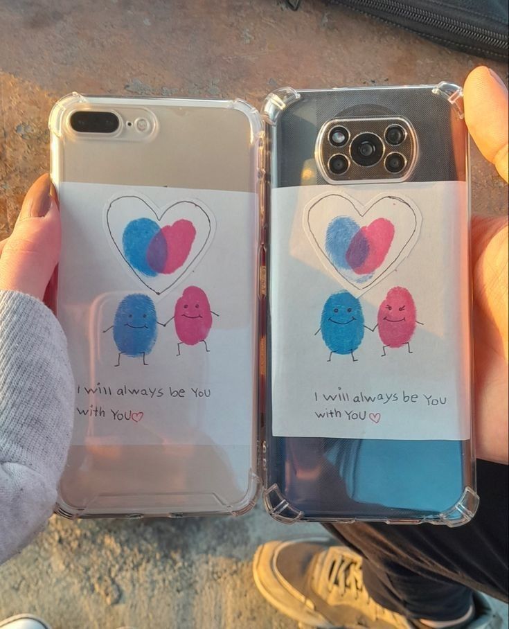 two people holding up cell phones that have hearts on them and one has a note attached to the back