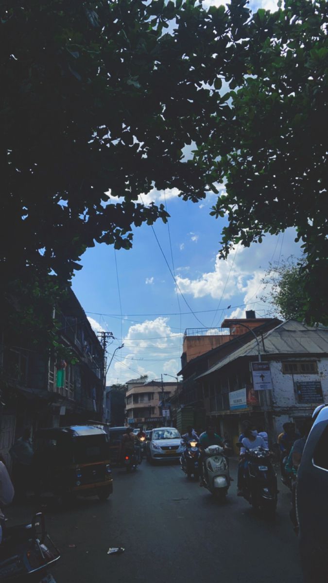 a street filled with lots of traffic under a cloudy blue sky and some people on motor bikes