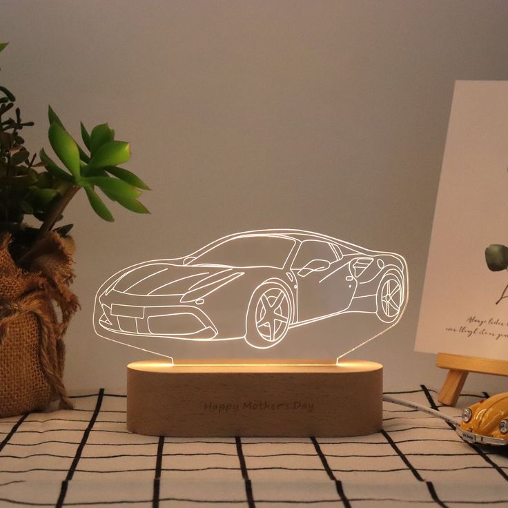 a car shaped lamp sitting on top of a table next to a potted plant