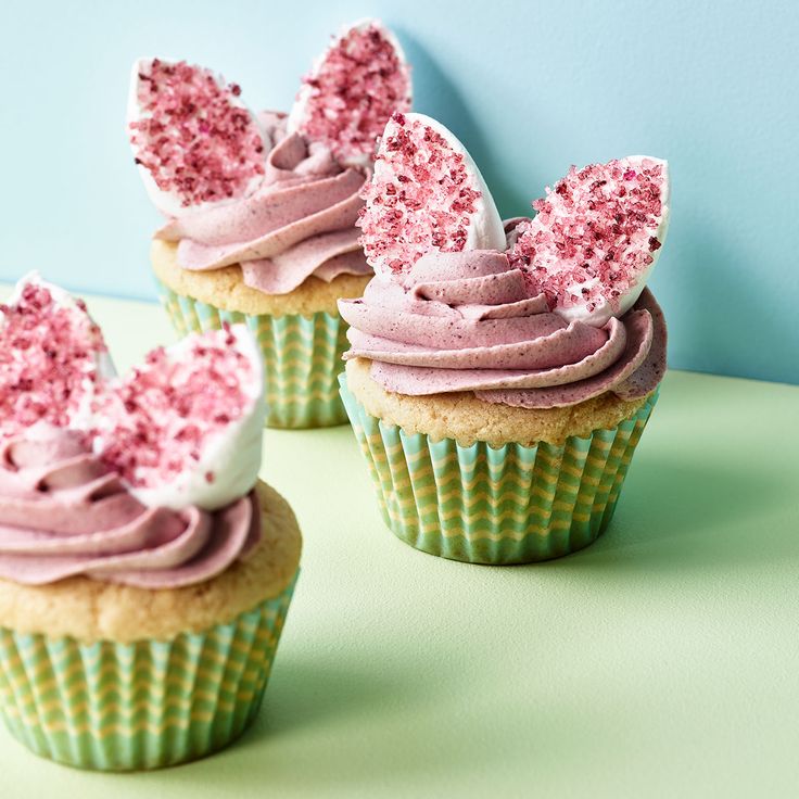 three cupcakes with pink frosting and sprinkles are on a green surface