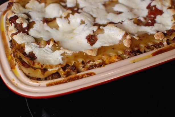 a square casserole dish with cheese and sauce on it, sitting on a red plate