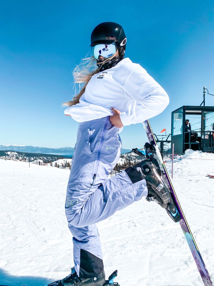 a woman in white snowsuit holding skis on top of the snow covered ground