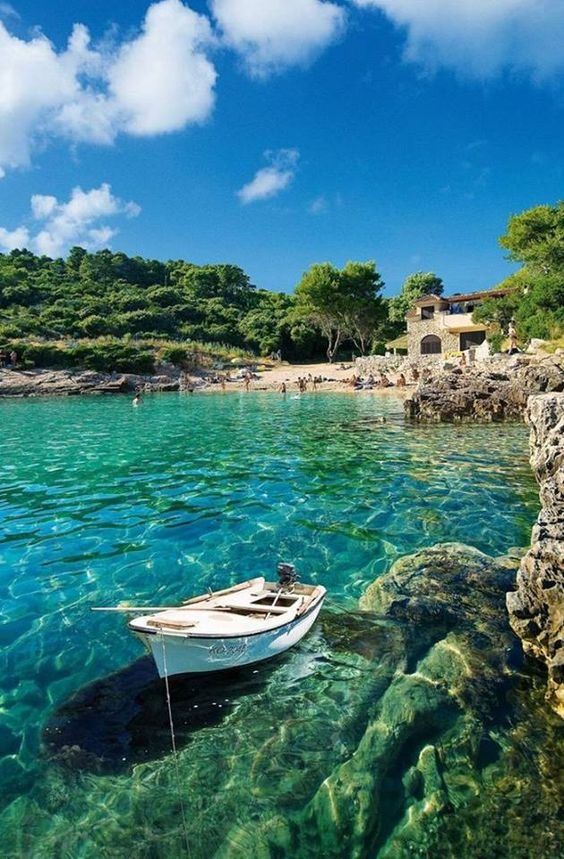 there is a boat that is sitting in the clear blue water near some rocks and trees