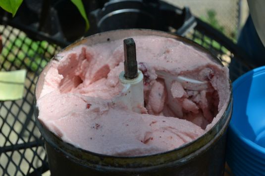 a bucket filled with pink ice cream next to blue plastic cups and a black wire fence