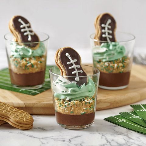 three desserts with football cookies and green frosting in glass cups on a tray