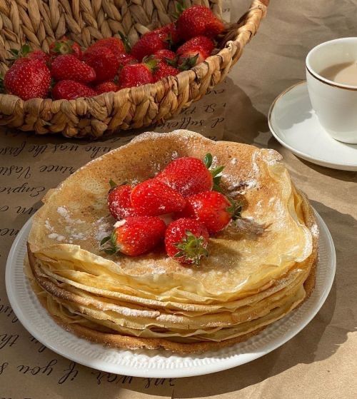 a stack of pancakes with strawberries on top next to a cup and saucer