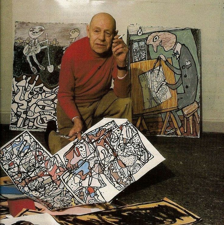 a man sitting on the floor next to paintings and talking on a cell phone in front of him