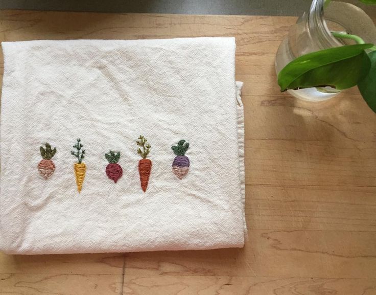 four carrots embroidered on a white towel next to a vase with green plants in it